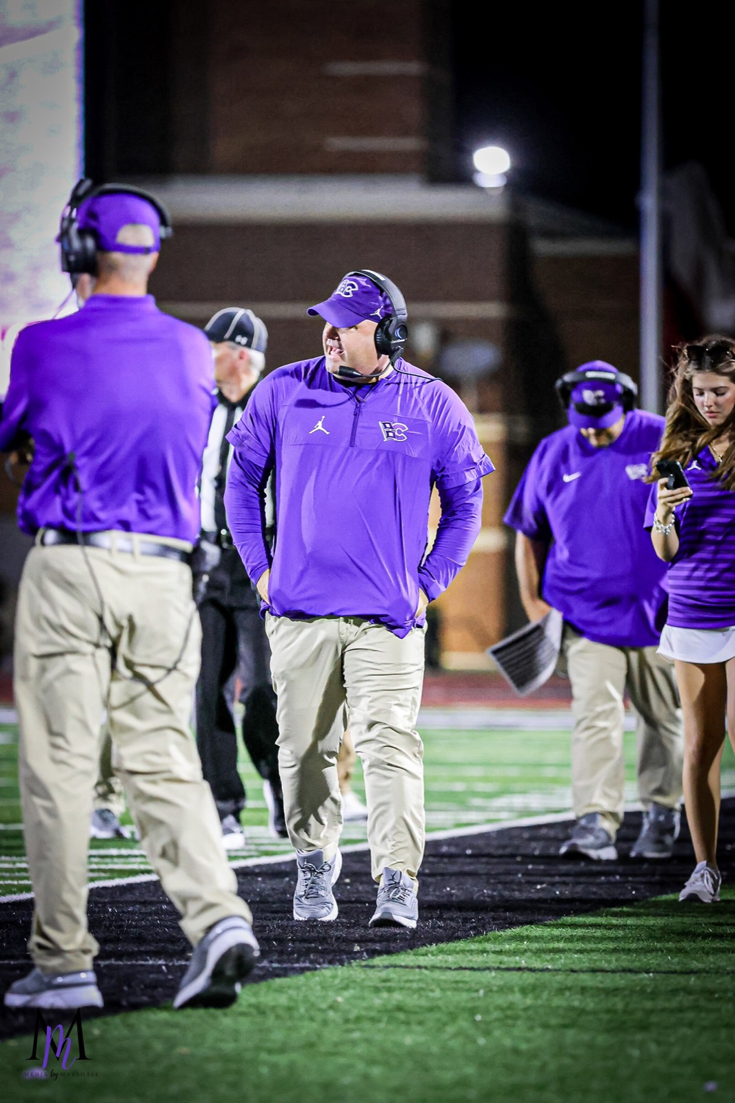 Head coach James Clancy patrols the sideline in his purple Hurricanes polo and headset at Turner Stadium
