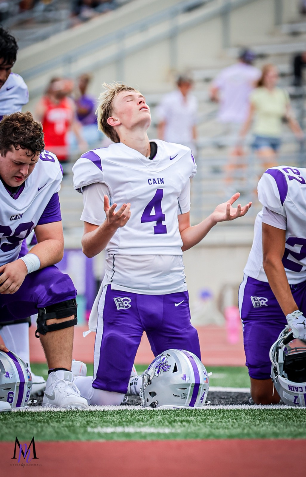 Senior kicker Sage DesAutels kneels in prayer with hands outstretched before kickoff