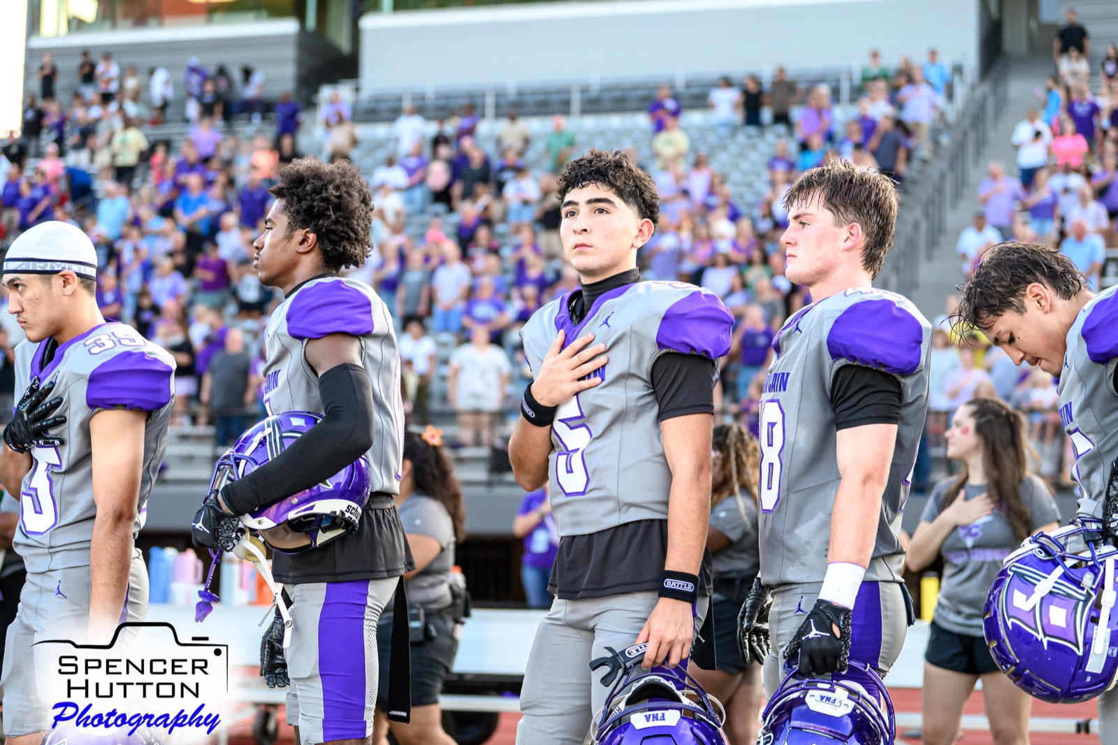 Klein Cain players stand along the sideline with helmets in hand during the national anthem