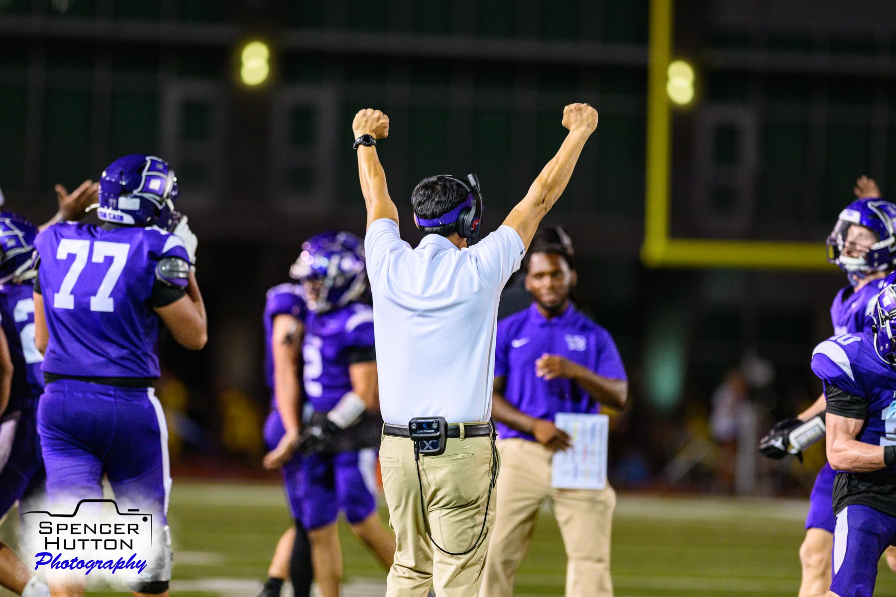 A Klein Cain coach signals touchdown with arms raised as players celebrate on the sideline